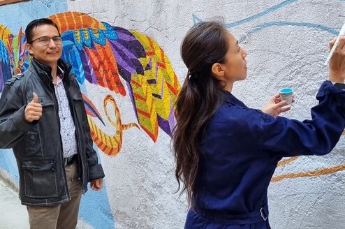 A man gives a thumbs up as a woman paints a wall.